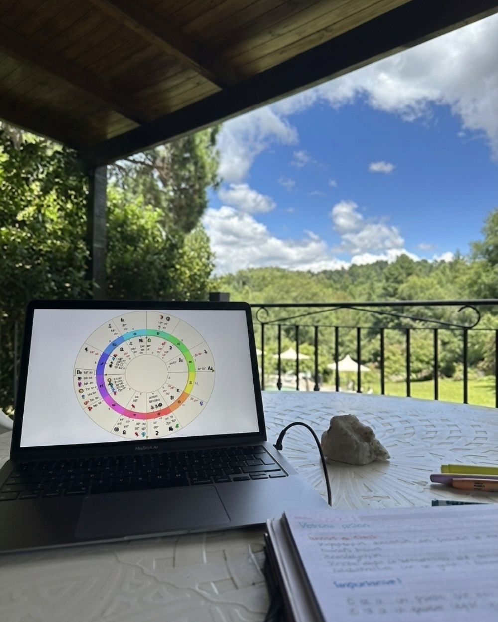 Notebook con una carta astrológica en pantalla, en una galería con vista al bosque